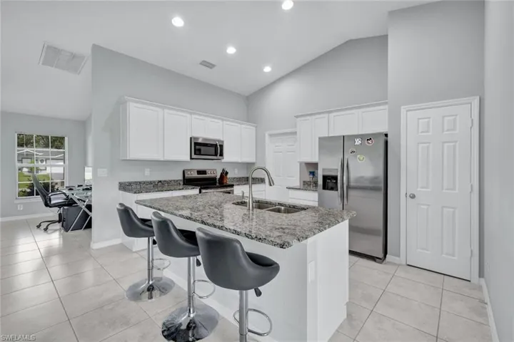 Kitchen with white cabinetry, appliances with stainless steel finishes, dark stone counters, a kitchen bar, and a kitchen island with sink