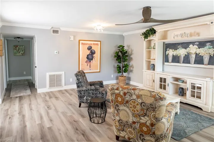 Living room featuring crown molding, baseboards, light wood-type flooring, and ceiling fan