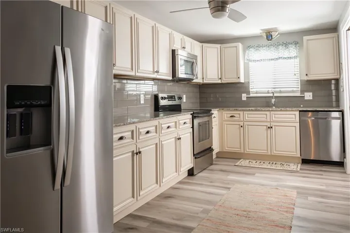 Kitchen with stainless steel appliances, a sink, a ceiling fan, light stone counters