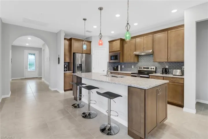 Kitchen featuring appliances with stainless steel finishes, light stone counters, a kitchen island with sink, sink, and pendant lighting