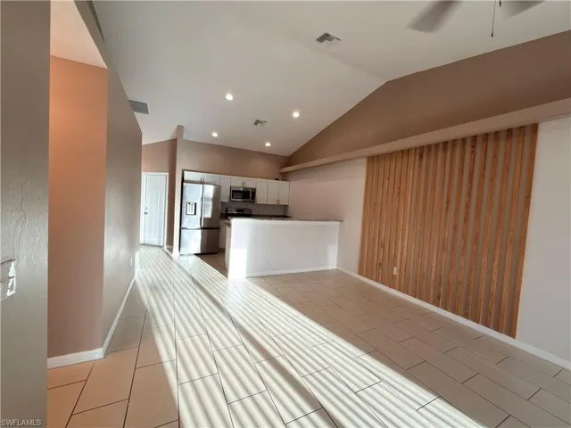 Kitchen featuring stainless steel appliances, lofted ceiling, white cabinetry, tasteful backsplash, and a peninsula