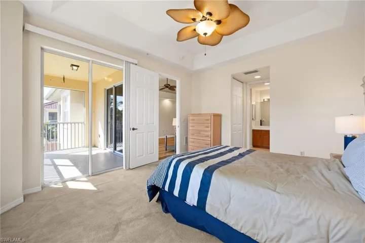 Bedroom featuring carpet, access to exterior, a ceiling fan, a tray ceiling, and ensuite bathroom