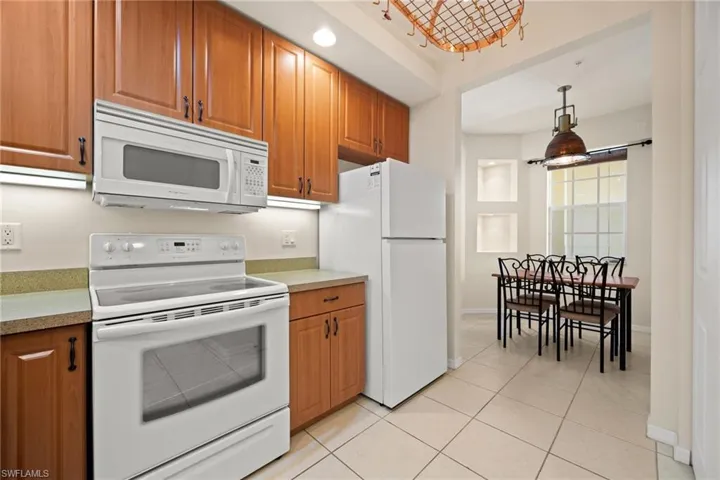 Kitchen to breakfast room with white appliances, wood finish cabinetry, light countertops, and pendant lighting