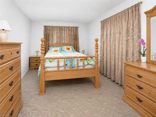 Carpeted room featuring a wooden four-poster bed, window with drapes, and white walls