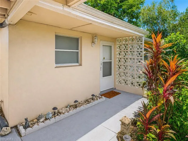 Stucco exterior with a covered entry, concrete walkway, and decorative privacy screen