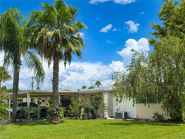 Single-story residence featuring a carport, a manicured lawn, and mature palm trees