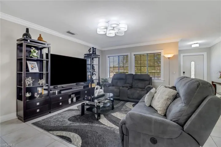 Tiled living room with ornamental molding, visible vents, baseboards, and a notable chandelier