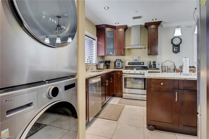 Kitchen with wall chimney exhaust hood, a sink, stacked washer and dryer, stainless steel appliances, and light stone counters