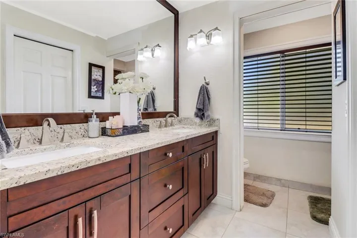 Full bath featuring toilet, double vanity, a sink, and tile patterned flooring