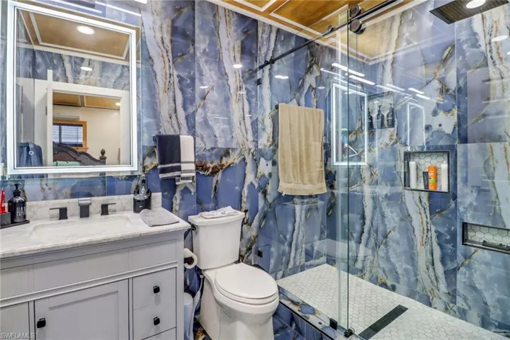 Full bathroom with toilet, a marble finish shower, vanity, and tile walls