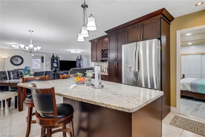 Kitchen featuring open floor plan, pendant lighting, light stone counters, and stainless steel refrigerator with ice dispenser