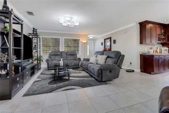 Living area featuring visible vents, baseboards, a notable chandelier, crown molding, and light tile patterned flooring