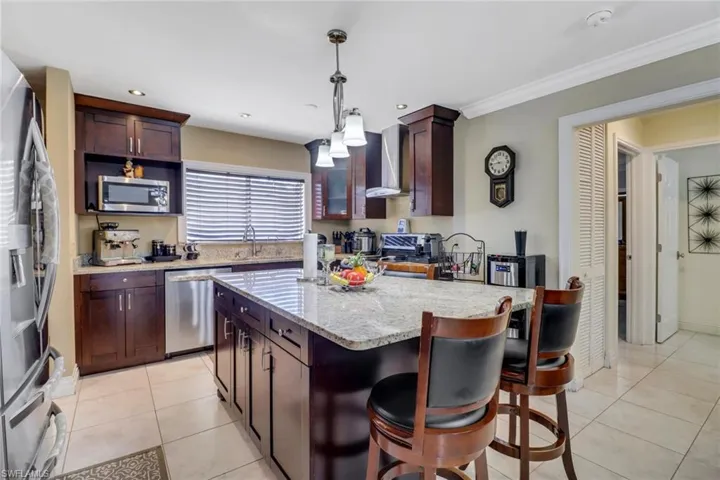 Kitchen featuring hanging light fixtures, a center island, wall chimney exhaust hood, stainless steel appliances, and light tile patterned flooring