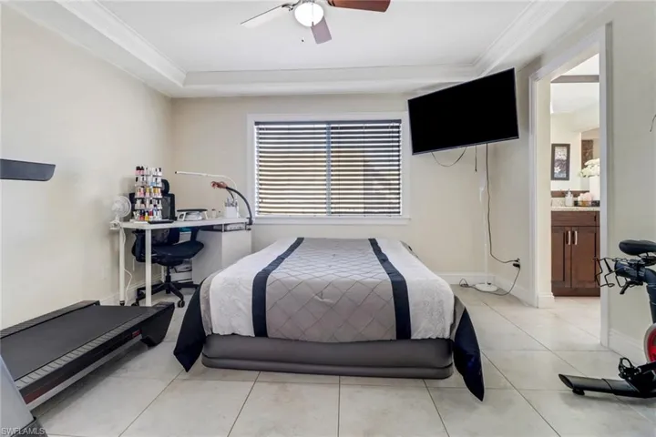 Bedroom with a ceiling fan, light tile patterned floors, ensuite bath, and ornamental molding