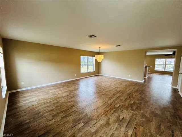 Empty room featuring dark wood-type flooring and suspended lighting
