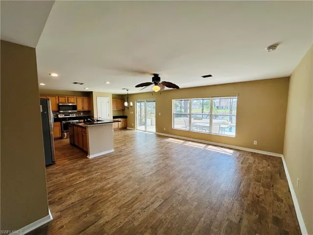 Kitchen featuring open floor plan, wood finish cabinetry, a kitchen island with sink, dark wood-style floors, and stainless steel appliances