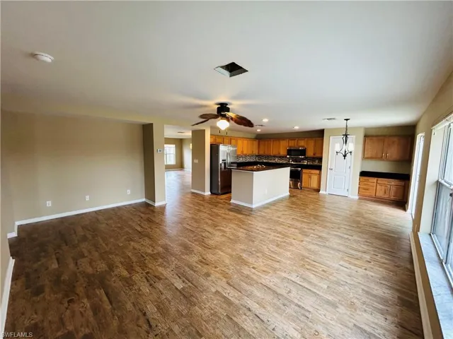 Kitchen featuring open floor plan, dark countertops, stainless steel appliances, a kitchen island, and dark wood-style floors