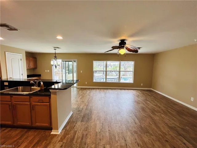 Kitchen with wood finish cabinets, open floor plan, dark wood-style floors, suspended lighting, and ceiling fan