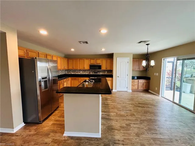 Kitchen featuring stainless steel appliances, an island with sink, light wood-style flooring, and suspended lighting