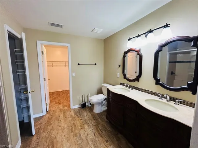 Bathroom with a spacious closet, dark wood-style floors, and double vanity