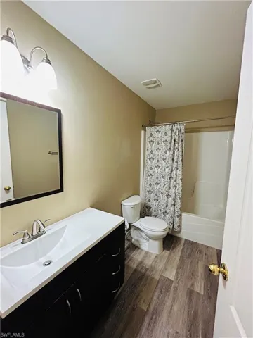 Full bath featuring vanity, shower / bath combo with shower curtain, and dark wood-type flooring