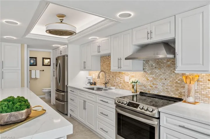 Kitchen featuring light tile patterned flooring, appliances with stainless steel finishes, white cabinets, and a raised ceiling