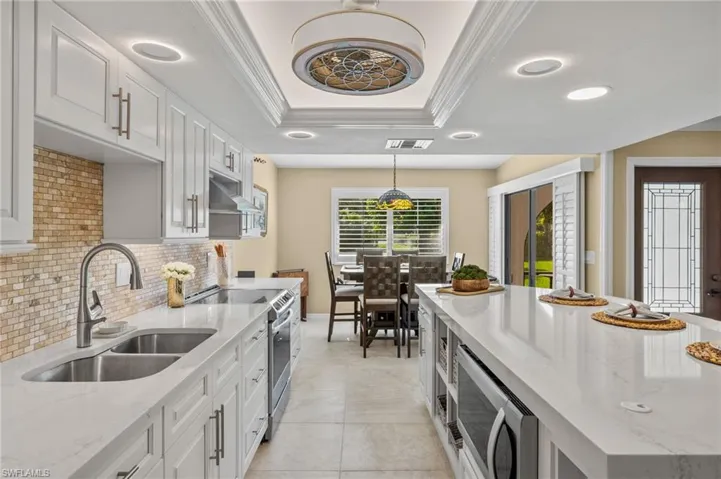 Kitchen featuring sink, hanging light fixtures, white cabinetry, electric range, and a raised ceiling