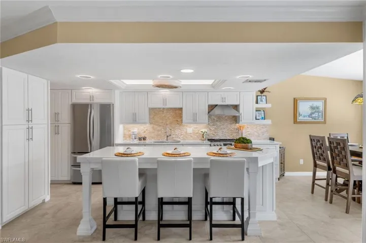 Kitchen featuring white cabinetry, backsplash, stainless steel refrigerator, and a kitchen island
