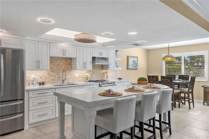 Kitchen featuring white cabinets, sink, stainless steel refrigerator, hanging light fixtures, and light tile patterned floors