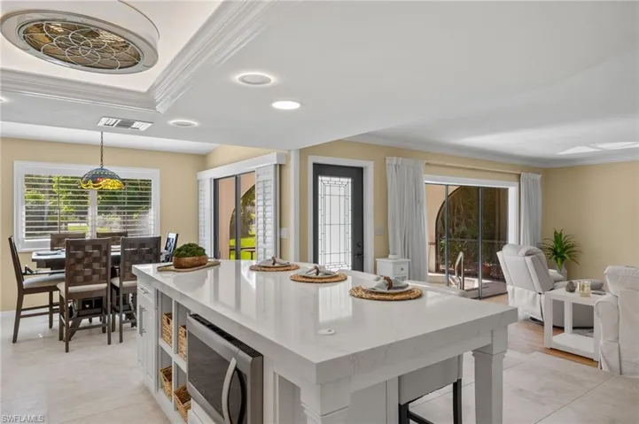 Kitchen featuring crown molding, light tile patterned floors, a kitchen island, a raised ceiling, and decorative light fixtures