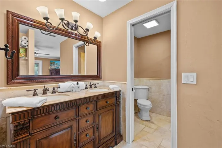 Bathroom featuring double sink vanity, toilet, ceiling fan, tile walls, and tile patterned floors