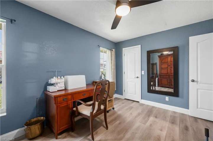 Office featuring a ceiling fan, a textured wall, light wood-style flooring, and baseboards