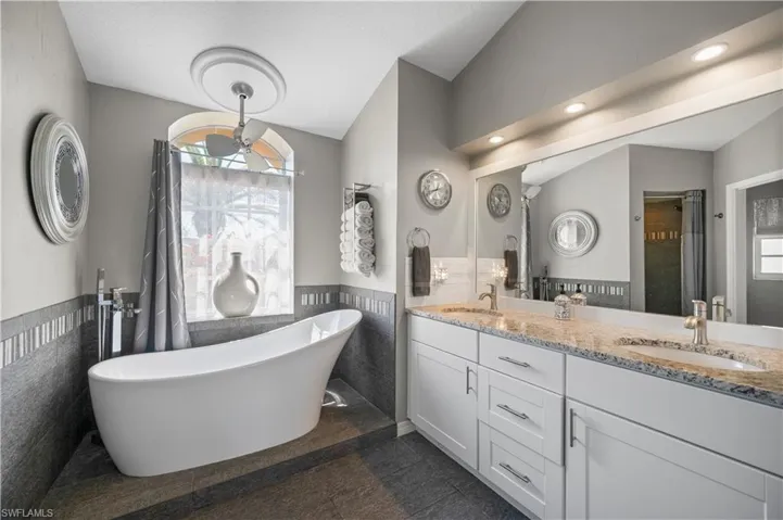 Bathroom with a sink, tile walls, vaulted ceiling, wainscoting, and double vanity