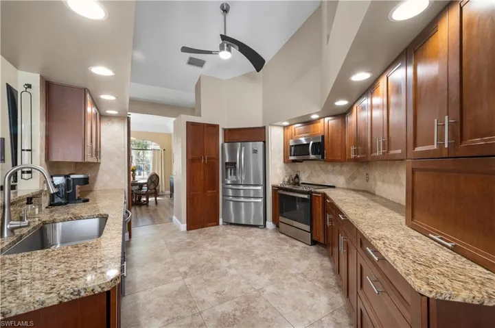 Kitchen featuring light stone counters, appliances with stainless steel finishes, decorative backsplash, and a sink