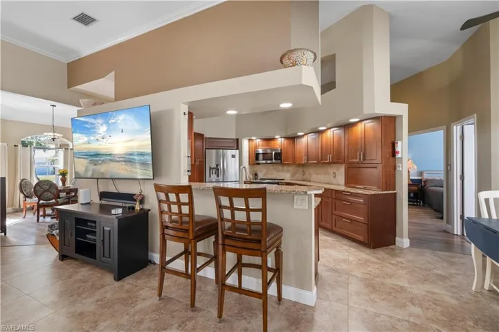 Kitchen with visible vents, decorative backsplash, appliances with stainless steel finishes, brown cabinets, and a kitchen breakfast bar