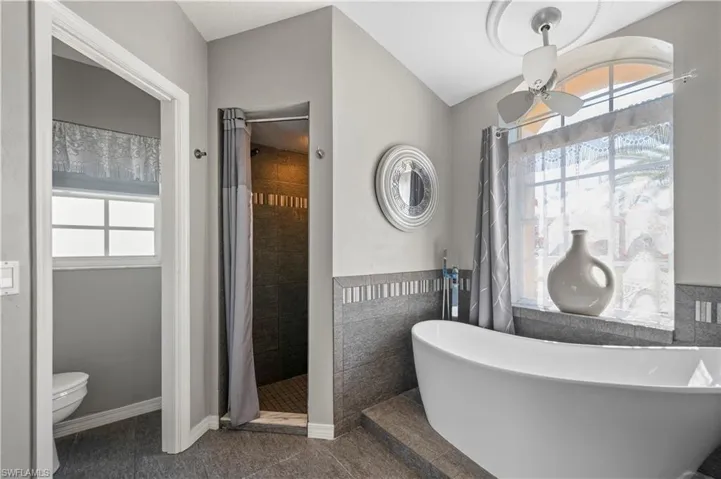 Full bathroom featuring tile walls, a soaking tub, toilet, a tile shower, and baseboards