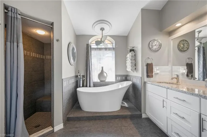 Full bathroom with a wainscoted wall, a tile shower, tile walls, and vanity