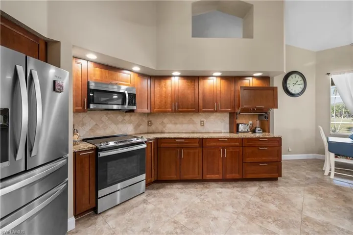 Kitchen with stainless steel appliances, brown cabinetry, light stone counters, and a high ceiling