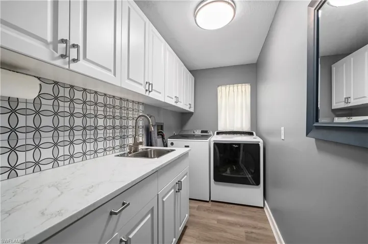 Laundry area featuring cabinet space, baseboards, washer and dryer, light wood-style floors, and a sink