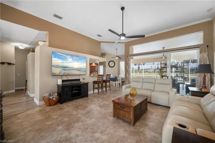 Living area with a ceiling fan, visible vents, ornamental molding, and baseboards