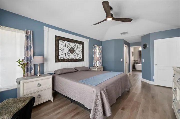 Bedroom with baseboards, visible vents, vaulted ceiling, and wood finished floors