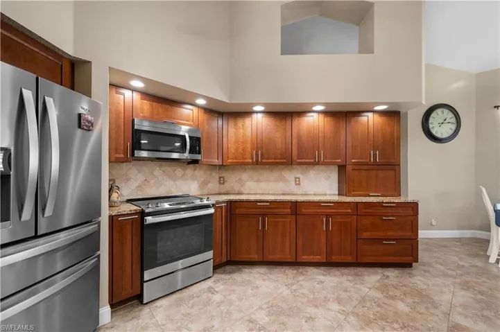 Kitchen featuring tasteful backsplash, baseboards, light stone counters, brown cabinets, and stainless steel appliances