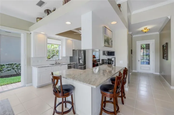 Kitchen with stainless steel appliances, crown molding, a sink, light tile patterned flooring, and a breakfast bar area