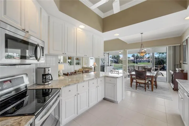 Kitchen with stainless steel appliances, ornamental molding, a peninsula, light tile patterned floors, and light stone counters