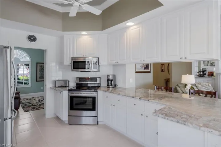 Kitchen with appliances with stainless steel finishes, white cabinetry, light tile patterned floors, crown molding, and a high ceiling