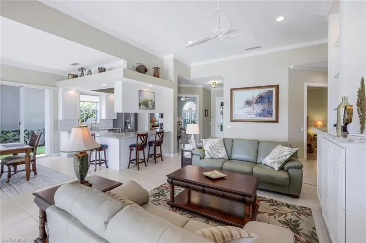 Living area with light tile patterned flooring, ornamental molding, and a ceiling fan