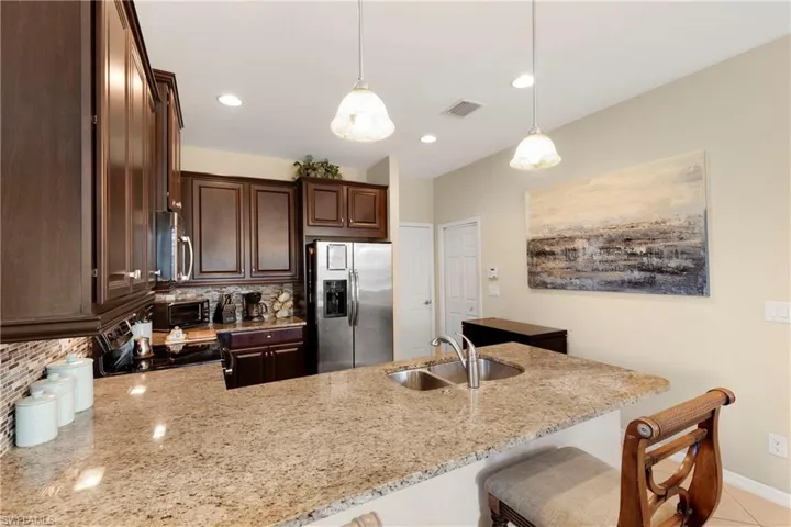 Kitchen with pendant lighting, stainless steel appliances, light stone countertops, and sink