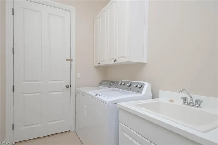 Washroom with light tile patterned floors, cabinets, independent washer and dryer, and sink