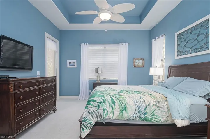 Bedroom with a raised ceiling, light colored carpet, and ceiling fan
