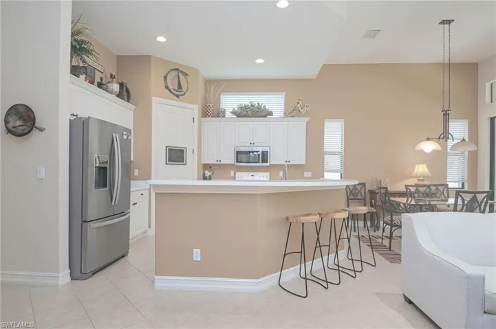 Kitchen with a breakfast bar area, decorative light fixtures, a center island with sink, appliances with stainless steel finishes, and white cabinetry